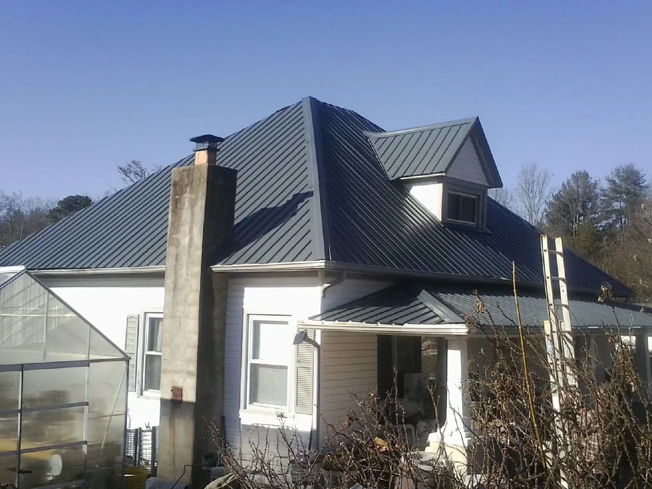 Dark blue standing seam metal roof on a white farmhouse with dormer — Slate & Tile Roof Repair by Roofing Brothers in Westwego