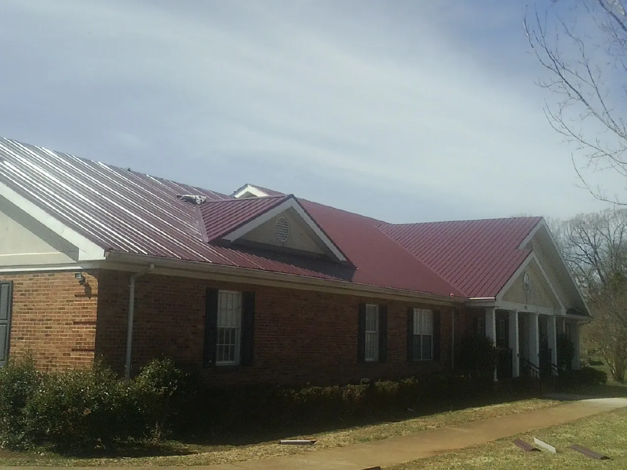 Red metal roof with gabled entries on a long brick building, from a Hail Damage Roof Repair job in Westwego