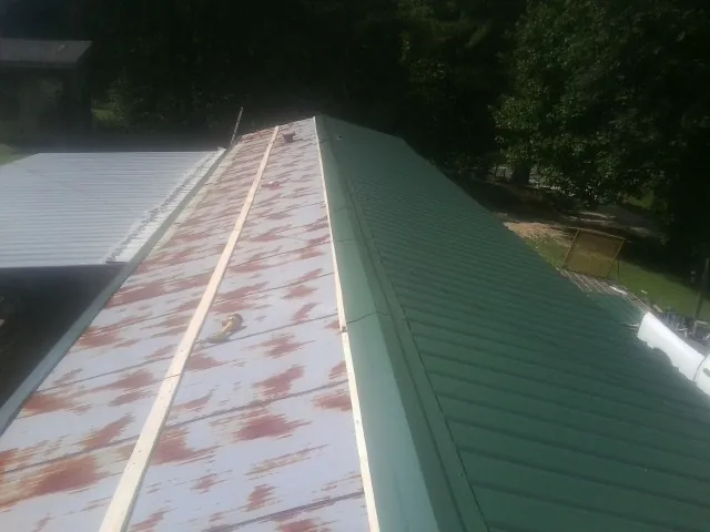 Old rusted panels beside newly installed green metal roofing — Wind Damage Roof Repair by Roofing Brothers in Westwego