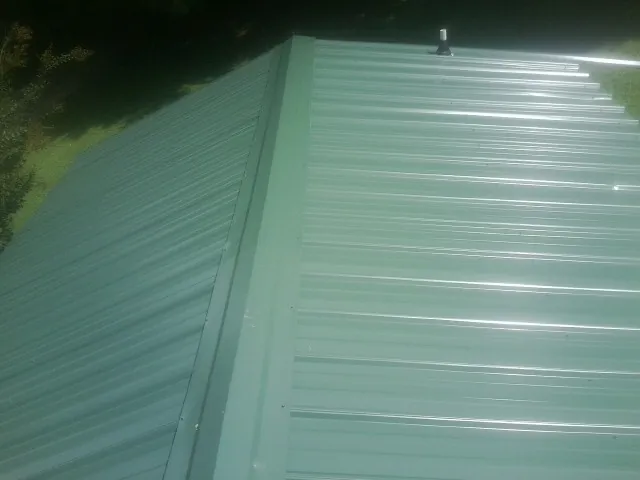 New green metal panels meeting at the ridge of a roof — Flat Roof Repair work by our crew in Westwego