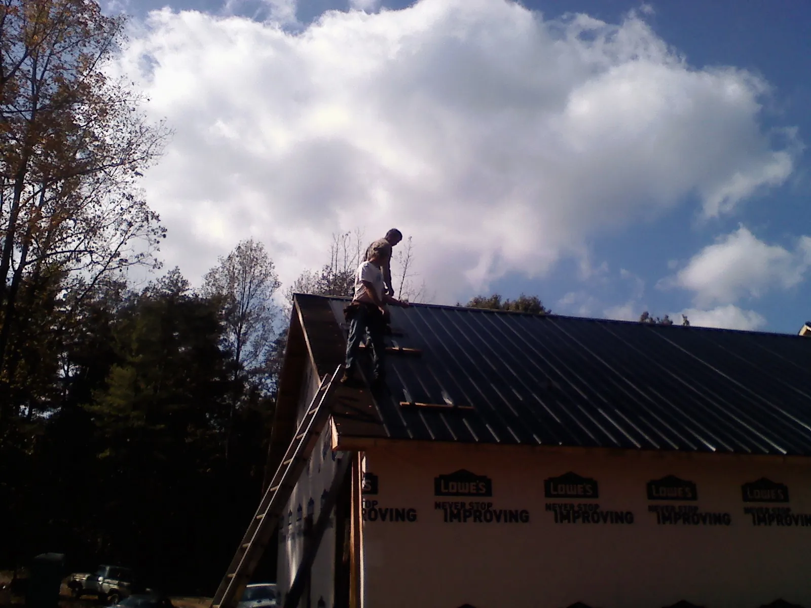 Roofer fastening dark metal panels high against a cloudy sky, from a Roof Inspection job in Westwego