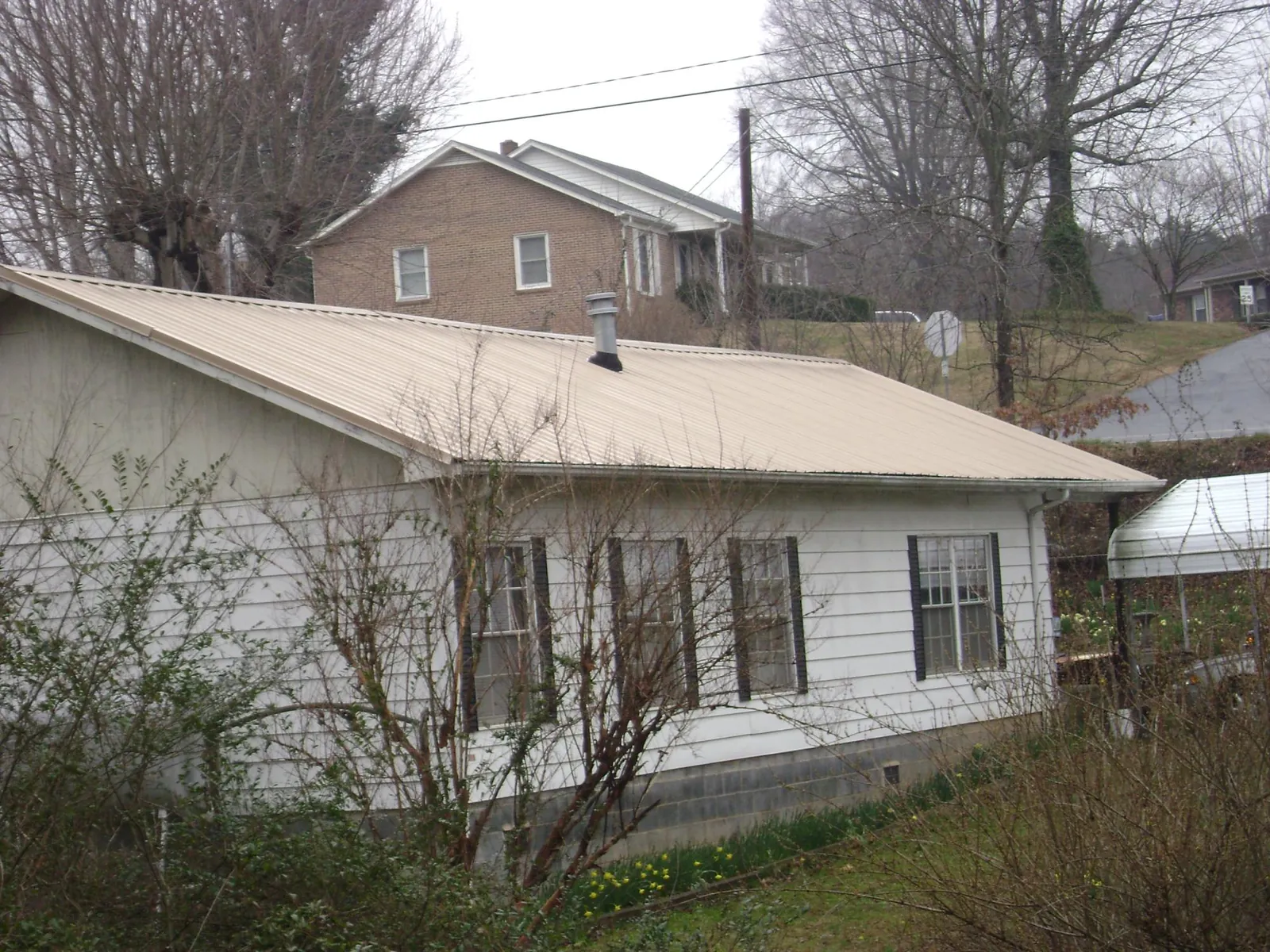 Tan metal roof on a white sided house set into a hillside — Commercial Roofing by Roofing Brothers in Westwego